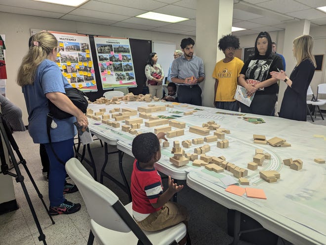 Designers and consultants from Urban Design Associates explain a revitalization plan with residents at Will Rogers Courts in Oklahoma City while a child interacts with a wooden block layout of the neighborhood.